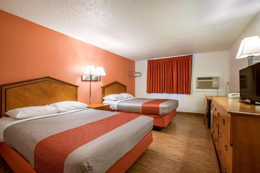 A hotel room with two beds, a desk, a television, and a window with curtains.