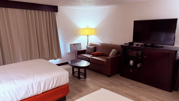 A hotel room with a bed, a sofa, a TV, a lamp, and a minibar. - Motel 6 Albert Lea (Albert Lea)