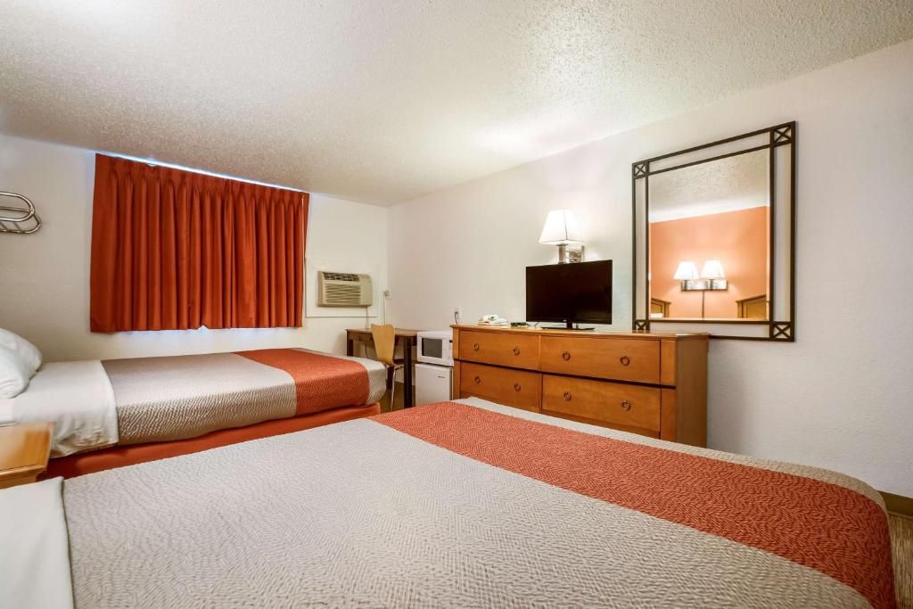 Hotellihuone, jossa on kaksi sänkyä, lipasto, televisio ja peili.