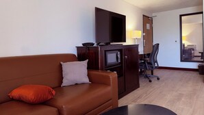 A hotel room with a brown leather sofa, a small black table, a flat-screen TV, a microwave, and a desk with a chair. - Motel 6 Albert Lea (Albert Lea)