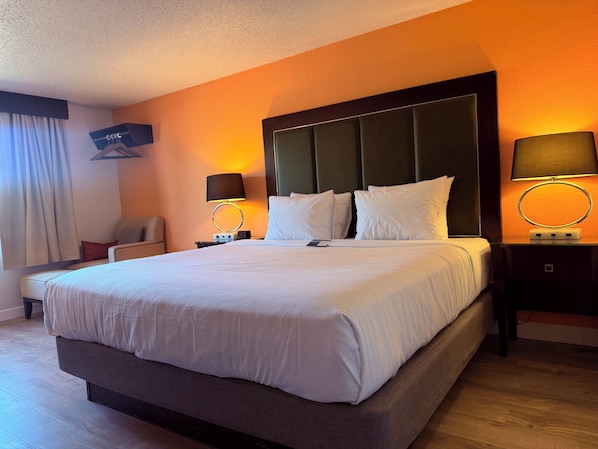 A hotel room with a large bed, two bedside tables, a chair, and a wall-mounted TV.