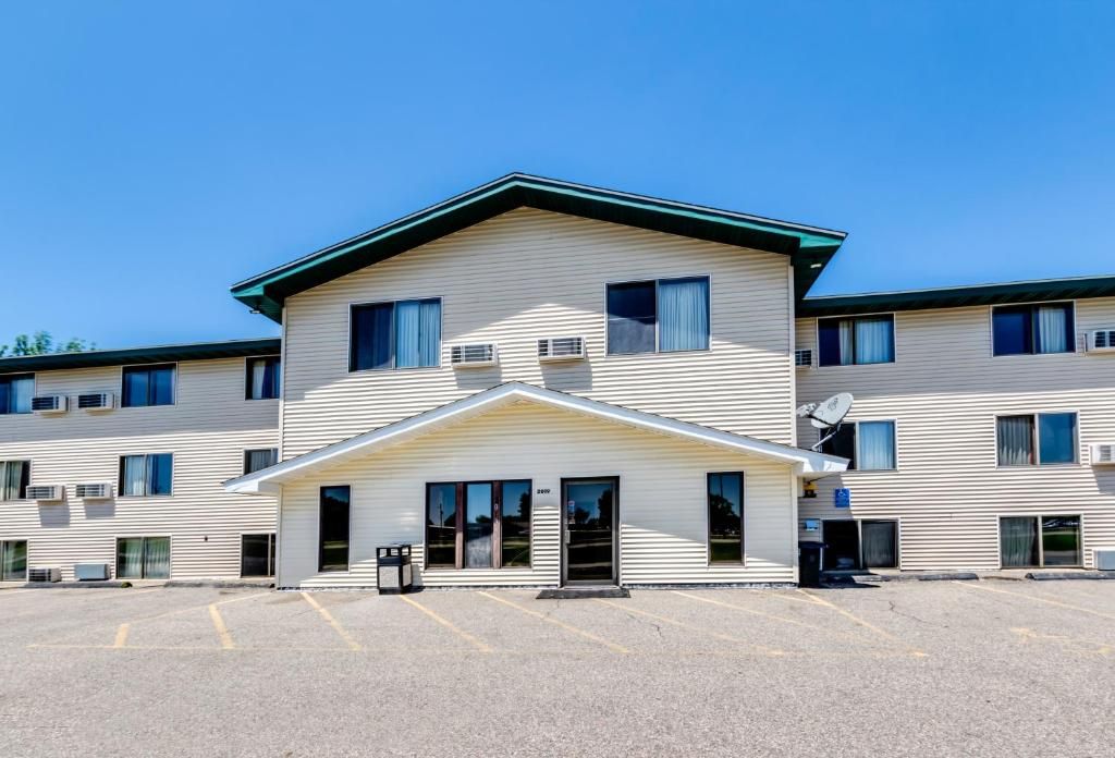 A multi-story hotel with a central entrance, air conditioning units, and a parking lot.