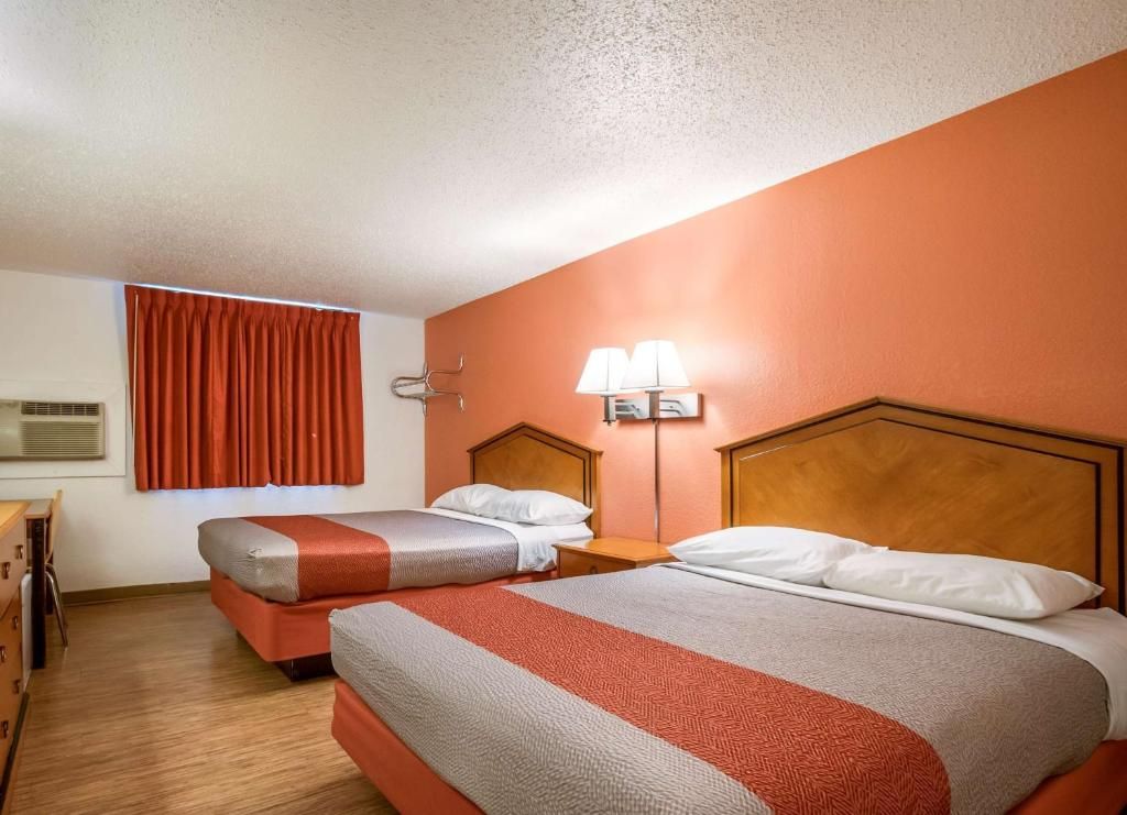 Een hotelkamer met twee bedden, een bureau en een raam met gordijnen.