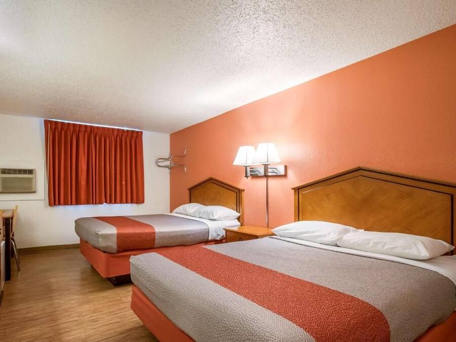 Een hotelkamer met twee bedden, een bureau en een raam met gordijnen.
