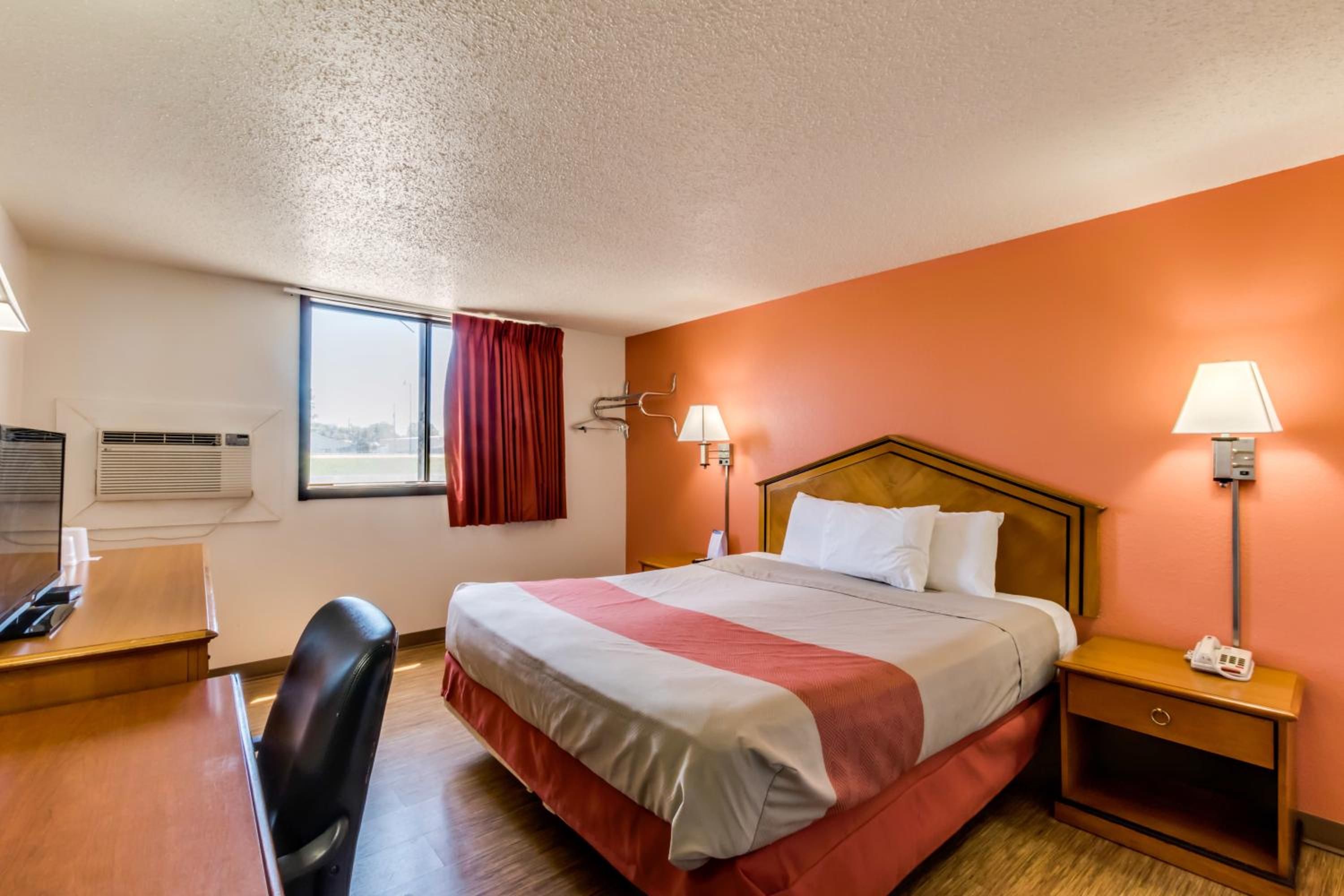 Ein Hotelzimmer mit Bett, Schreibtisch, Stuhl, Nachttischlampen und einer Klimaanlage.
