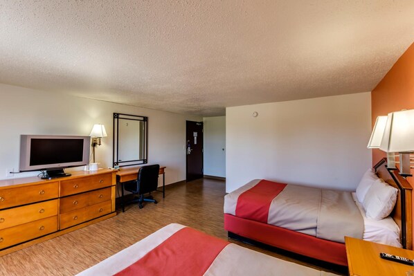 Una habitación de hotel con cama, escritorio con televisor, silla y cómoda.