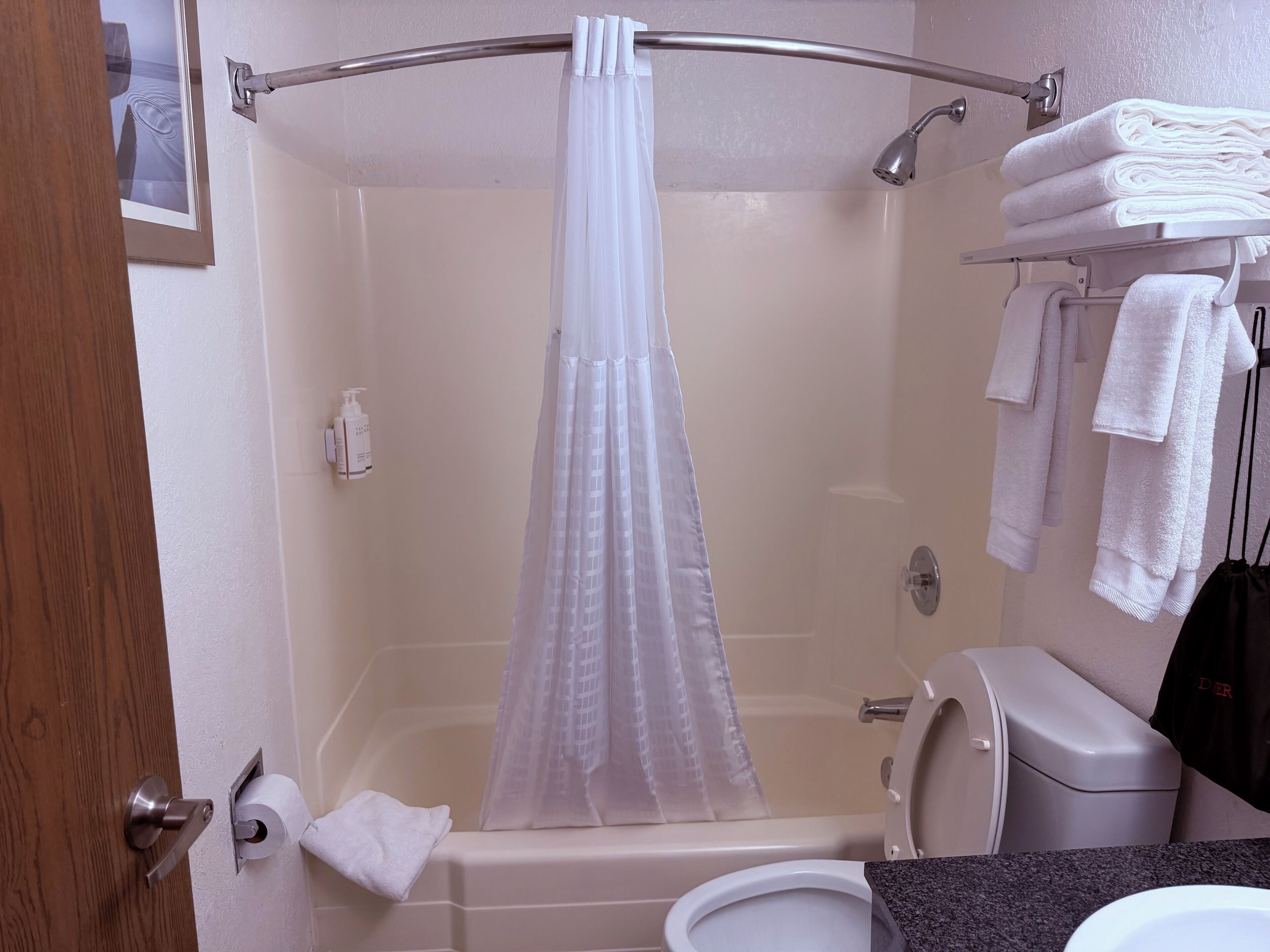 A shower with a white curtain, a toilet, a sink, and a towel rack with towels.