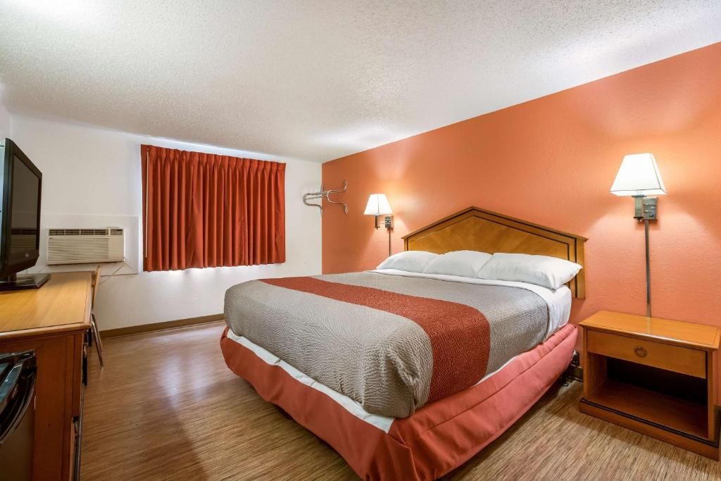 Habitación de hotel con una cama, un escritorio, un televisor, un equipo de aire acondicionado y dos lámparas fijadas a la pared.