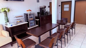 A conference room with a long table, chairs, a refrigerator, a coffee machine, and a TV screen displaying food. - Motel 6 Albert Lea (Albert Lea)