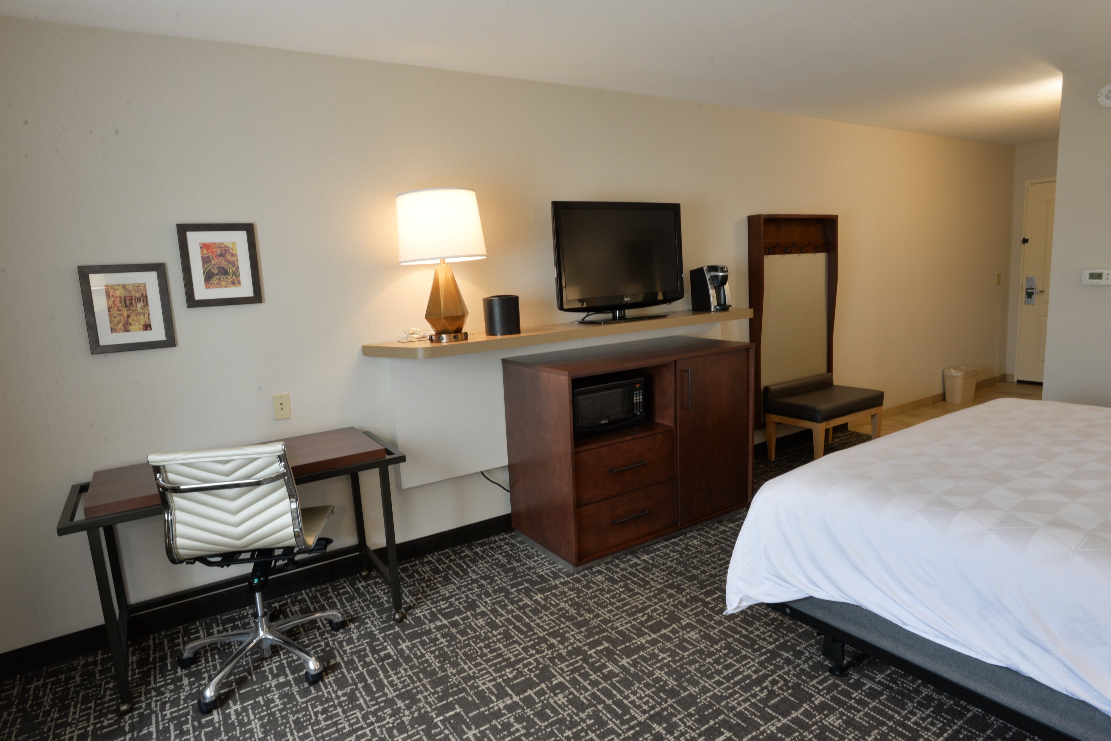 A hotel room with a bed, desk, chair, television, and a mirror.
