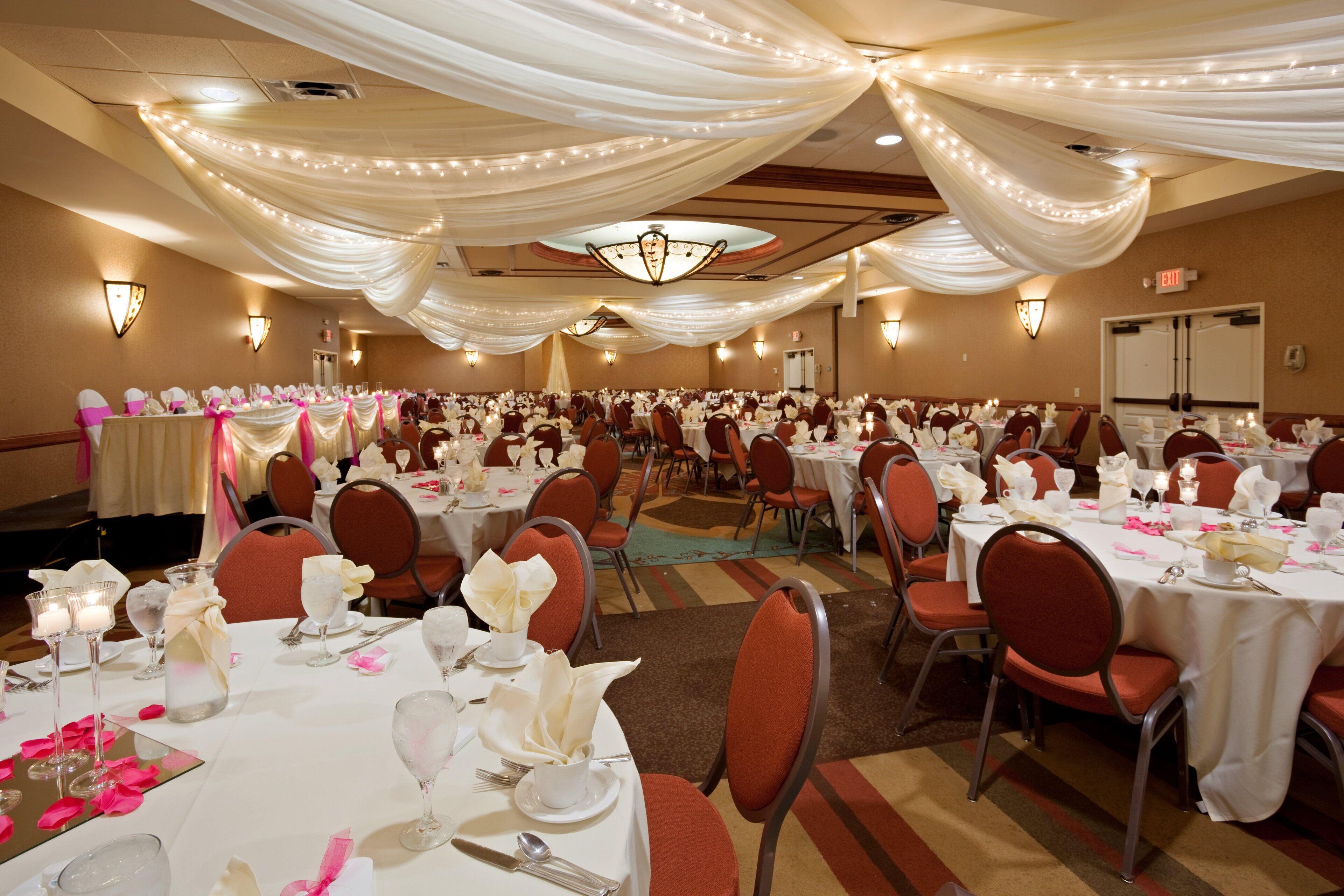 Une salle de banquet avec des tables rondes, des chaises rouges et des nappes blanches.