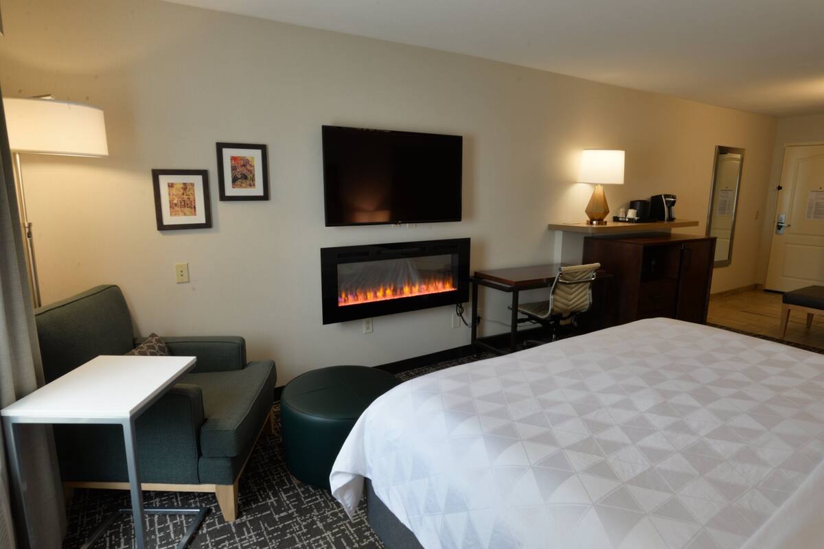 A hotel room with a bed, a TV mounted on the wall, a fireplace, a desk, and a couch.