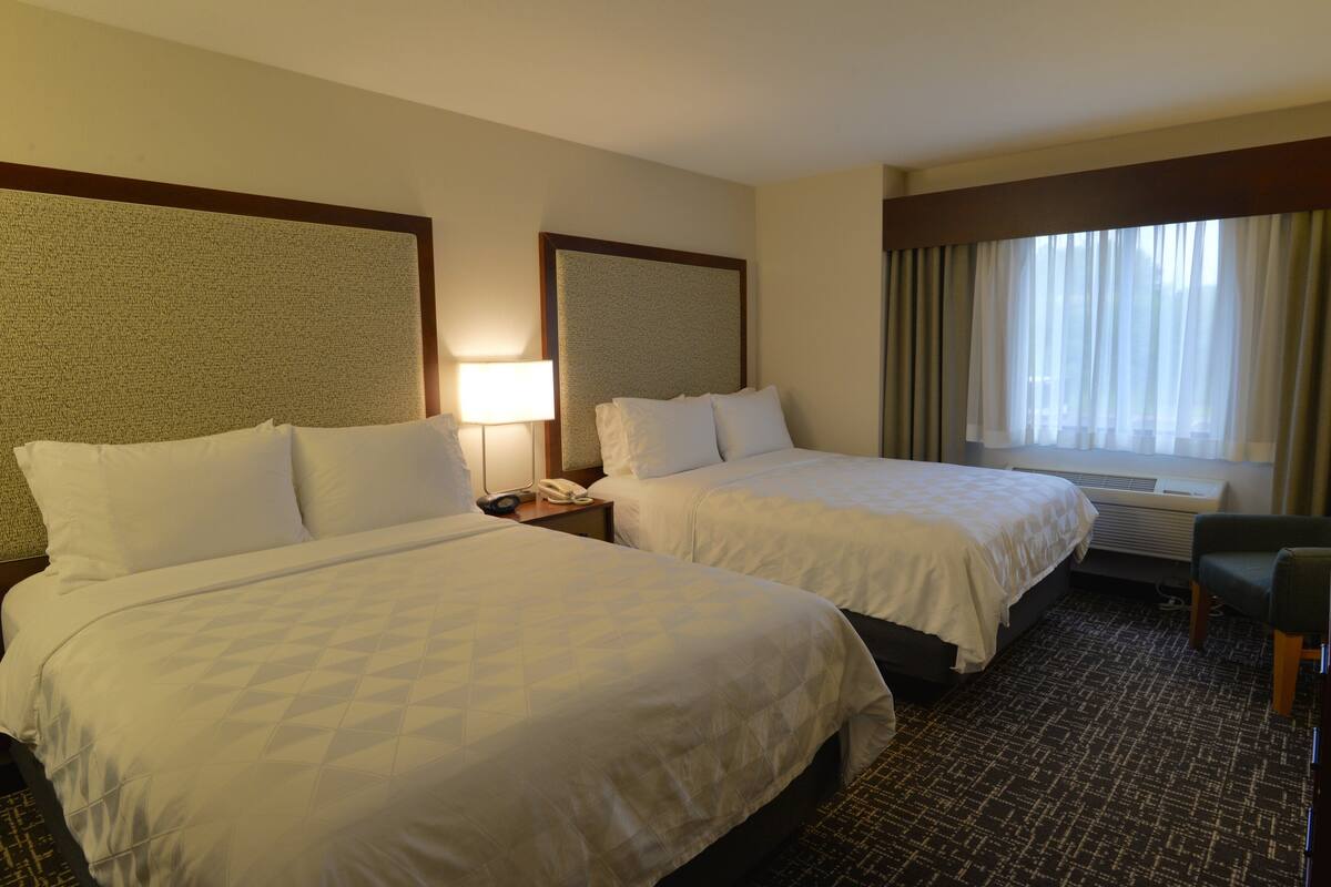 A hotel room with two beds, a desk, a chair, and a large window with curtains.