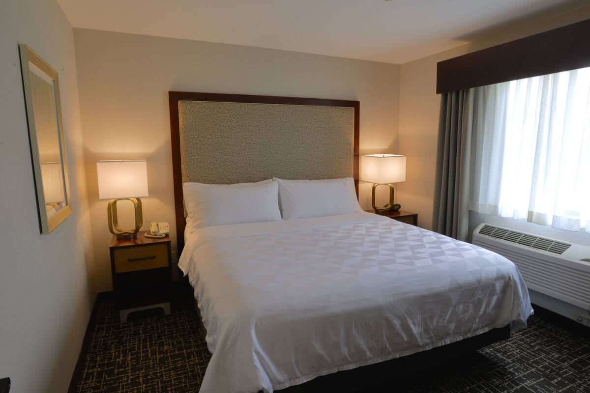 A hotel room with a large bed, two bedside tables with lamps, a mirror, and a window with curtains.
