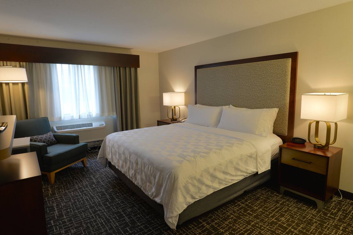 A hotel room with a large bed, two bedside tables with lamps, a chair, and a desk.
