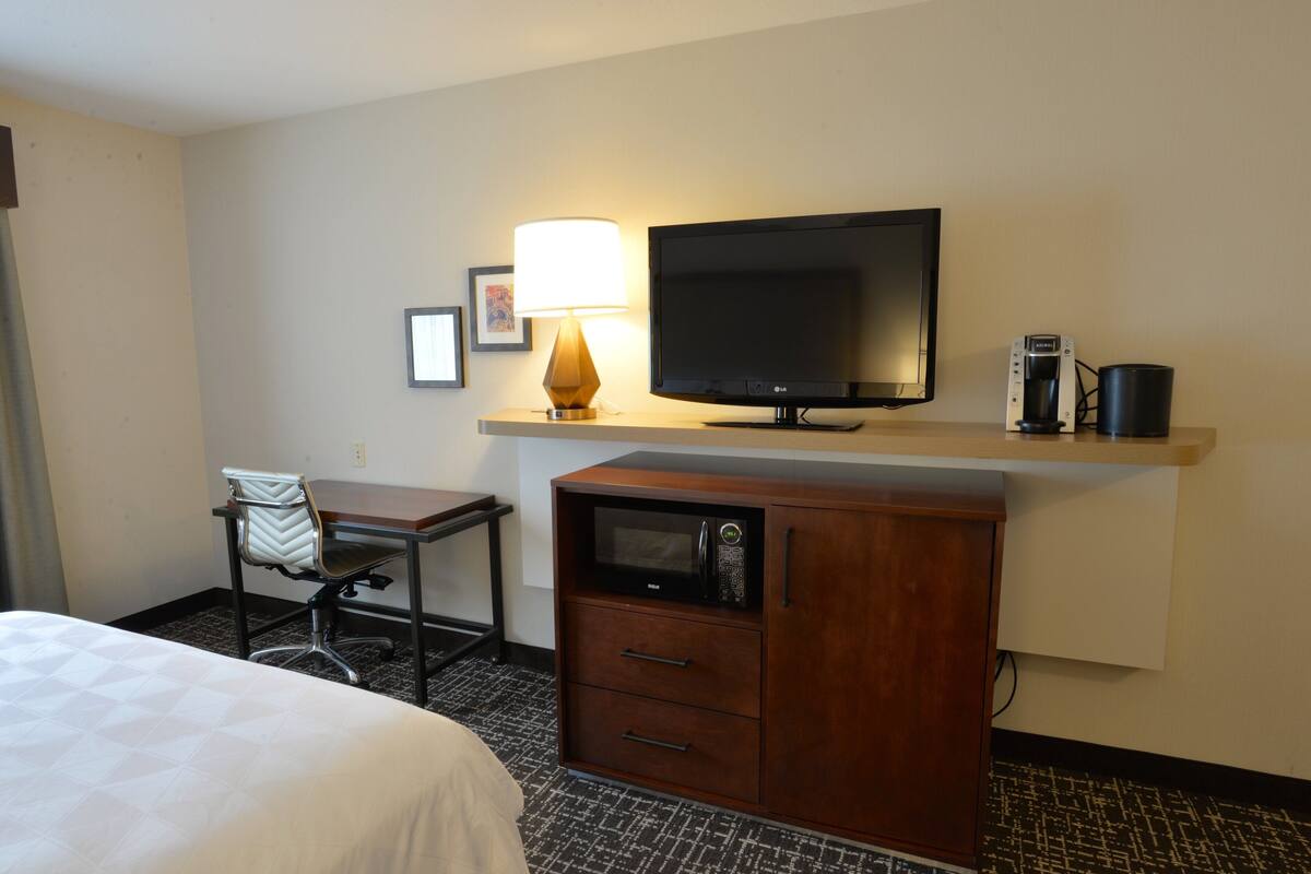 A hotel room with a bed, a desk with a lamp, a television, a coffee maker, and a microwave.