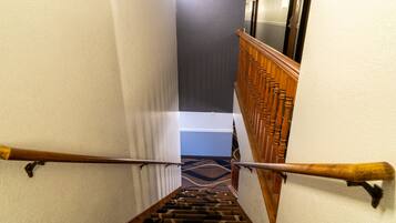 Una escalera con barandilla de madera, peldaños alfombrados y vista a un pasillo con una puerta al final.