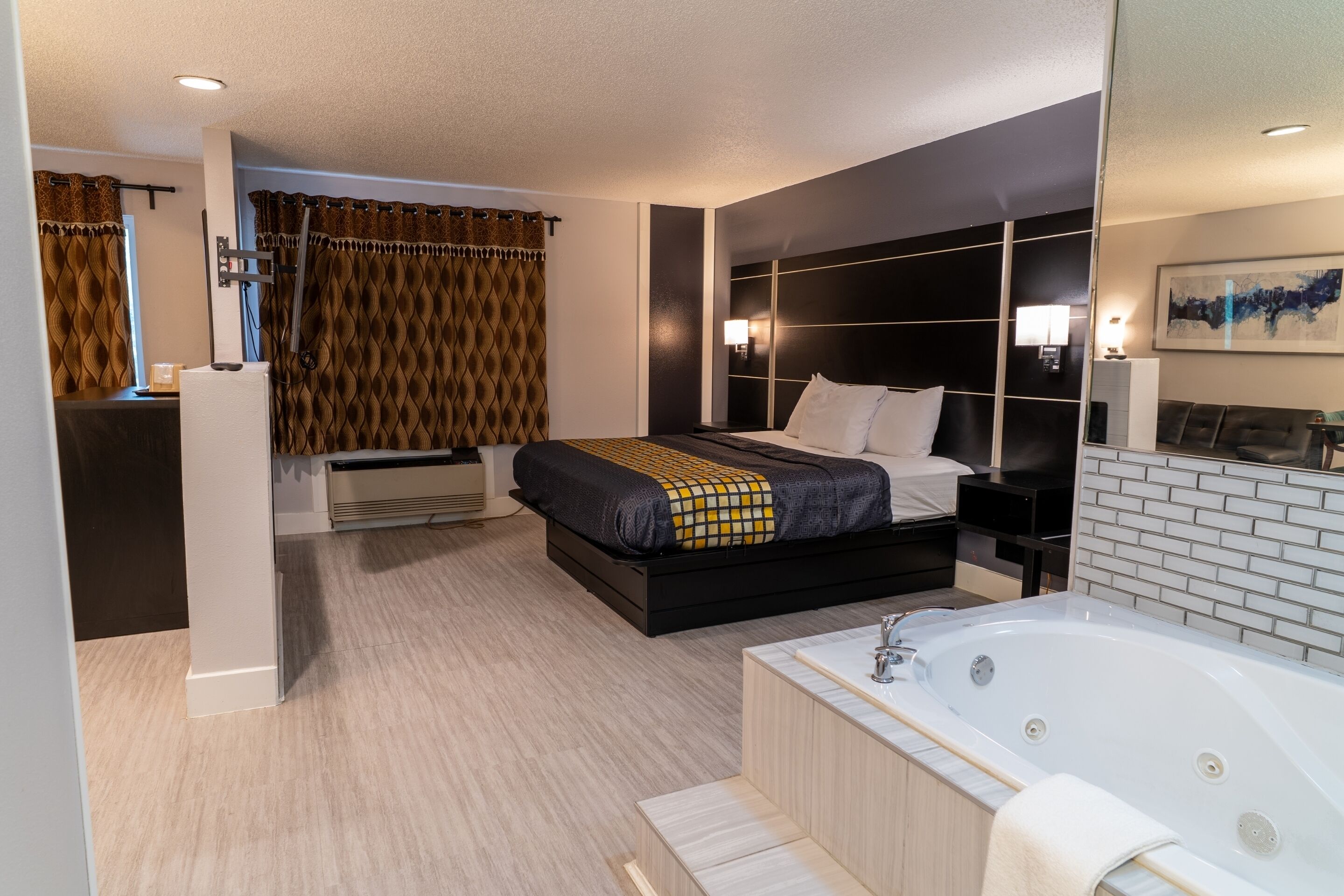 A modern hotel room with a large bed, a separate bathroom with a bathtub, and a separate seating area.