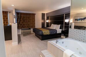 A modern hotel room with a large bed, a separate bathroom with a bathtub, and a separate seating area. - Coratel Inn & Suites by Jasper Hastings (Hastings)