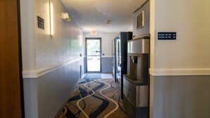 A hotel hallway with an exit sign, a refrigerator, and directional signs for rooms.