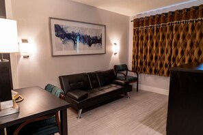 Una sala moderna con un sofá de cuero, una mesa de comedor con sillas, un cuadro abstracto enmarcado, una lámpara de pared y una cortina estampada.