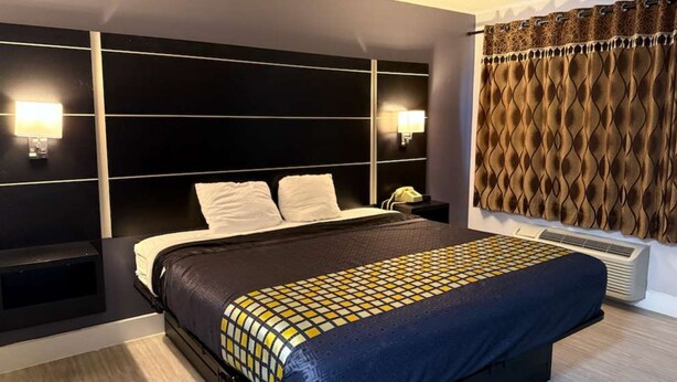 Una camera d'albergo moderna con un letto grande, una testiera con illuminazione integrata, un comodino con una lampada e una tenda a motivi.