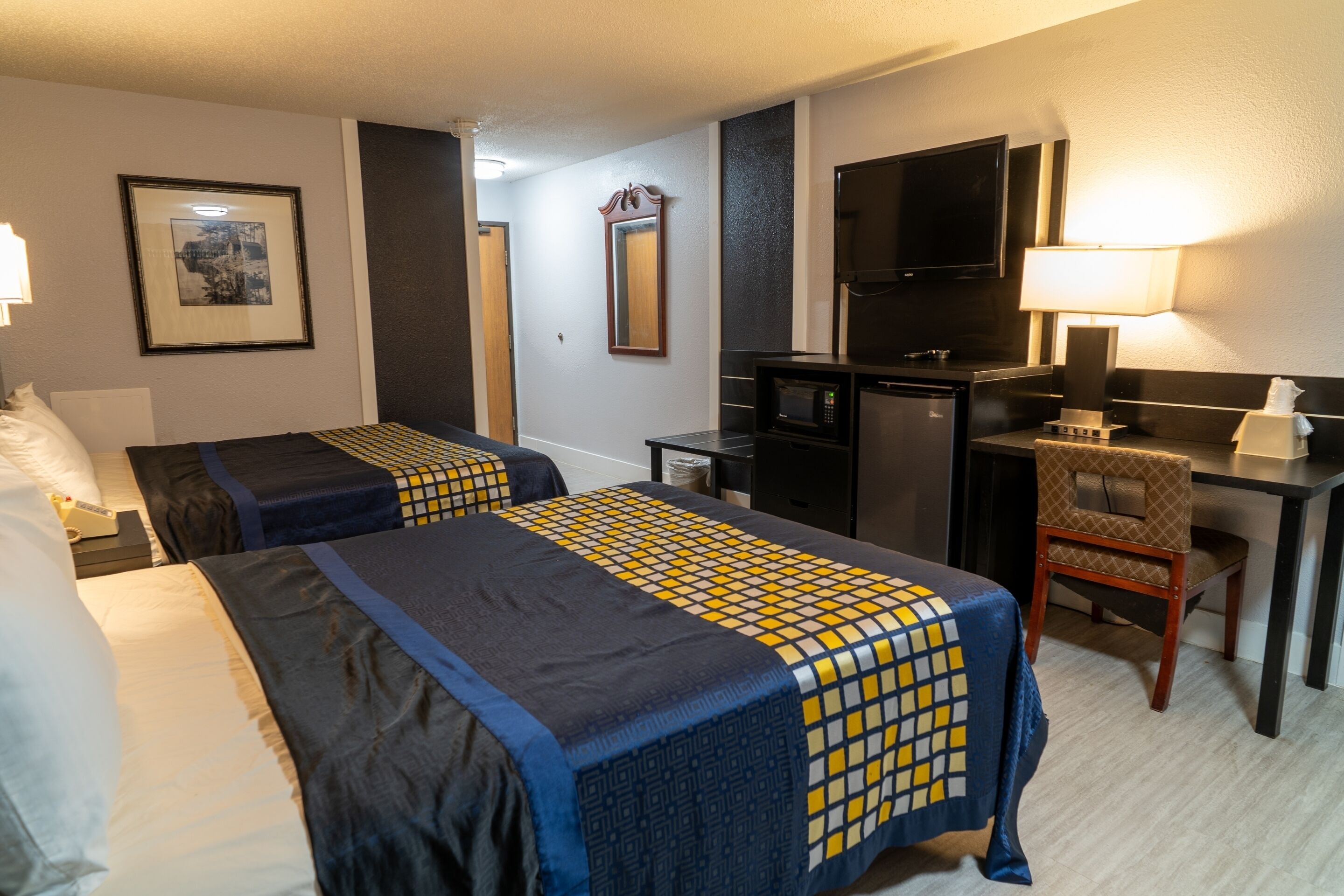 A hotel room with two beds, a desk, a chair, a television, and a microwave.