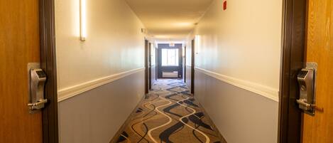 A hotel hallway with carpeted floors, doors on both sides, and a light fixture on the ceiling.