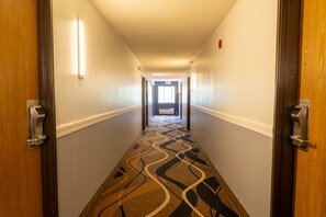 A hotel hallway with carpeted floors, doors on both sides, and a light fixture on the ceiling. - Coratel Inn & Suites by Jasper Hastings (Hastings)