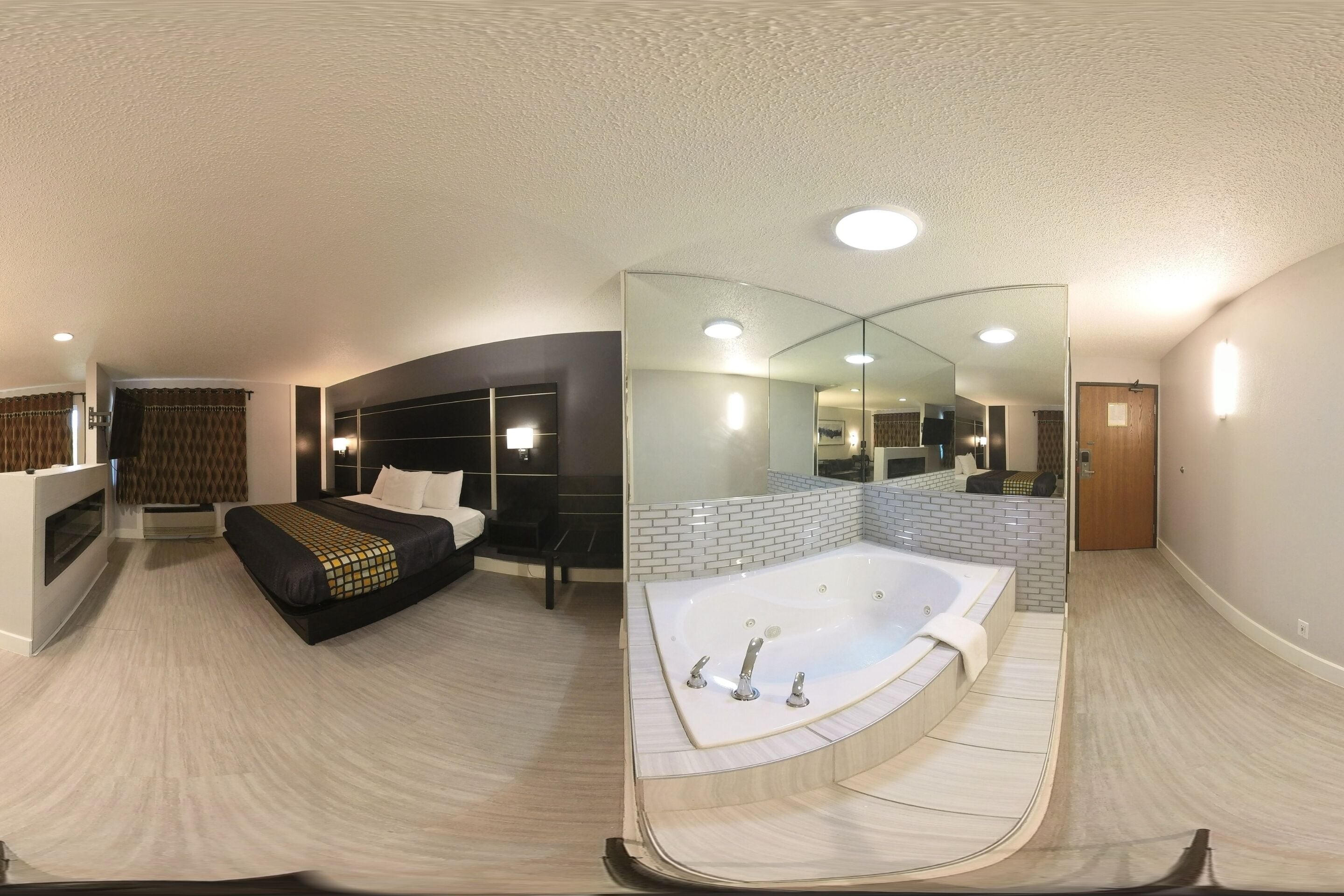 A modern hotel room with a large bed, a separate sitting area, a walk-in closet, and a separate bathroom with a bathtub.
