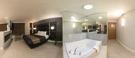 A modern hotel room with a large bed, a separate sitting area, a walk-in closet, and a separate bathroom with a bathtub.