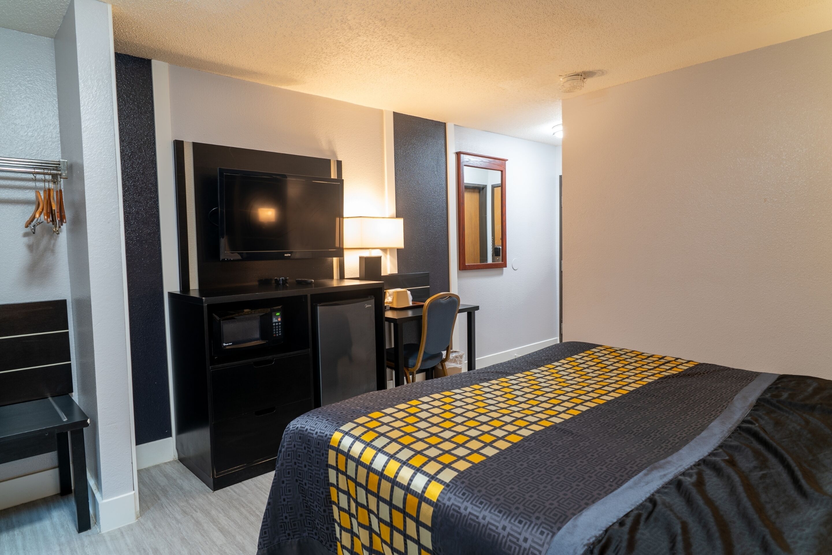 Habitación de hotel con una cama, un escritorio con televisor, un refrigerador pequeño y una silla.