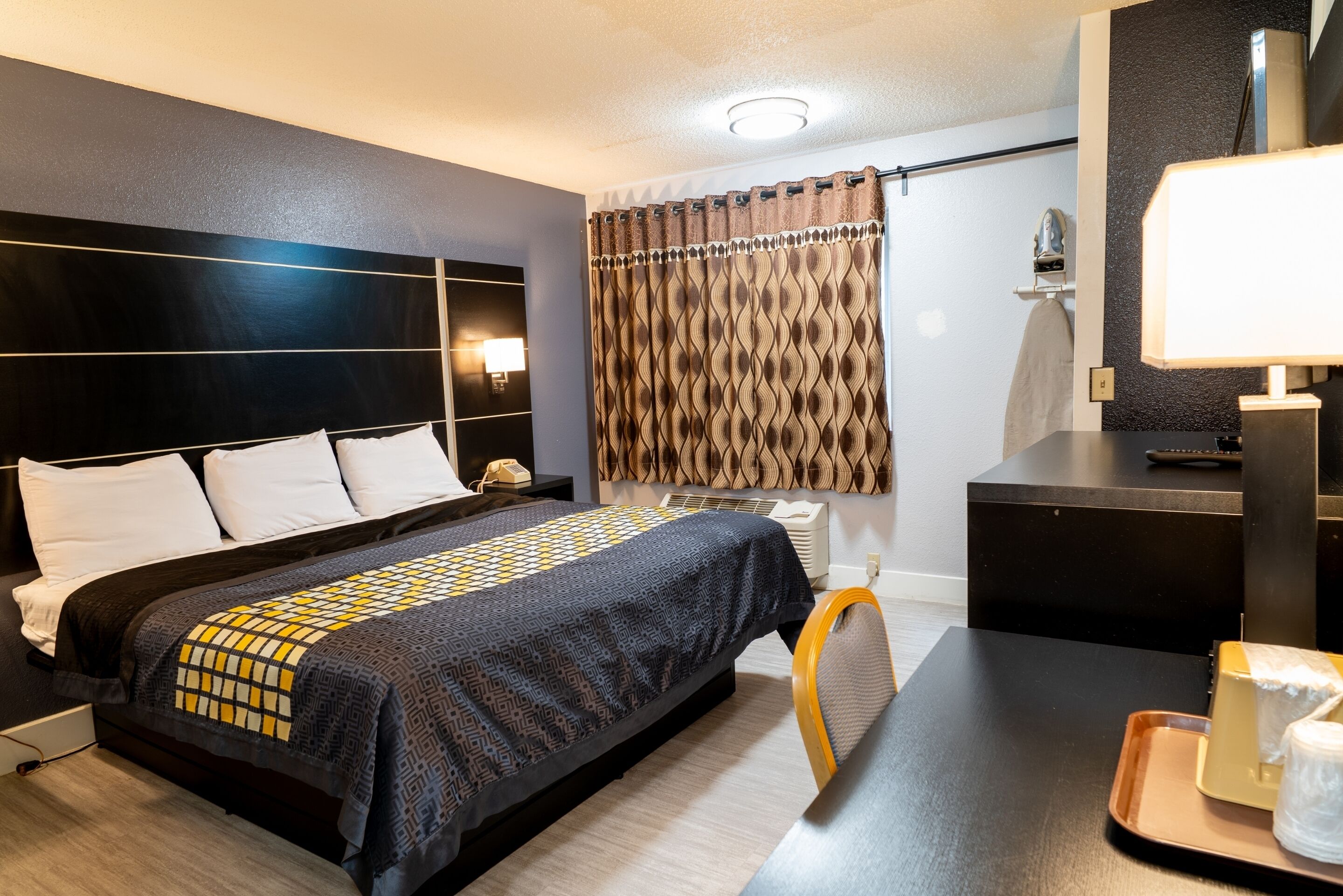 Una habitación de hotel con una cama grande, un escritorio, una silla, un espejo y una cortina.