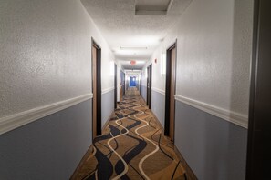 A hotel hallway with a patterned carpet, doors on both sides, and an exit sign on the ceiling. - Coratel Inn & Suites by Jasper Hastings (Hastings)