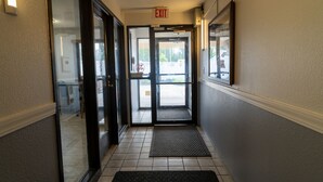 L’entrée d’un hôtel, avec des portes en verre, un sol carrelé, un paillasson noir et un panneau de signalisation indiquant la sortie, fixé au mur.