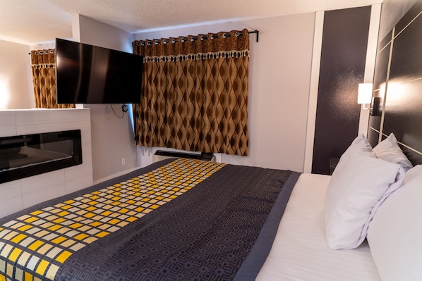 Habitación de hotel con cama, televisor de pantalla plana montado en la pared, mueble empotrado para la televisión, colcha estampada y cortina con diseño ondulado.