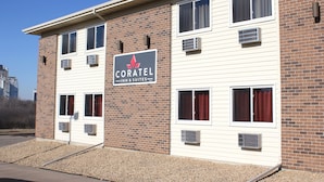 A hotel with a sign reading "CORATEL INN & SUITES." It features a brick facade with multiple windows and air conditioning units.