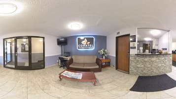 A hotel lobby with a reception desk, a sofa, a coffee table with newspapers, and a glass door entrance.