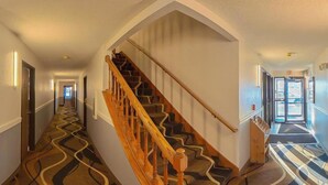 Un corridoio di un albergo con una scala in legno, un tappeto decorato e un segnale di uscita.
