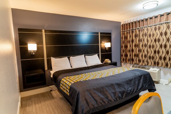 A hotel room with a large bed, bedside lamps, a telephone, a heater, and a patterned curtain.