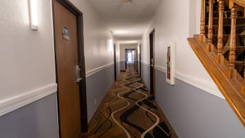 A hotel hallway with a patterned carpet, wooden doors, and a staircase with wooden balusters.