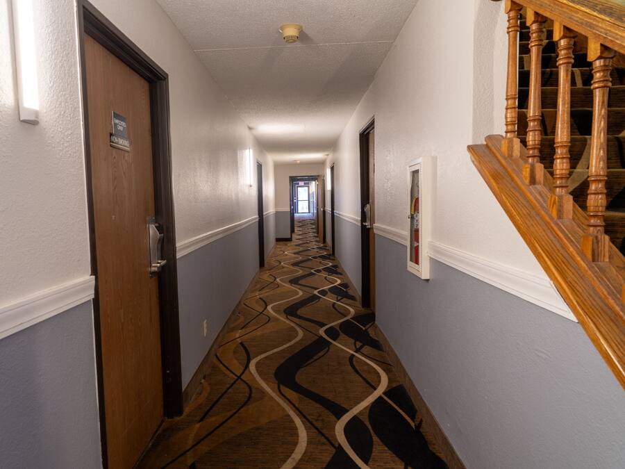 A hotel hallway with a patterned carpet, wooden doors, and a staircase with wooden balusters.