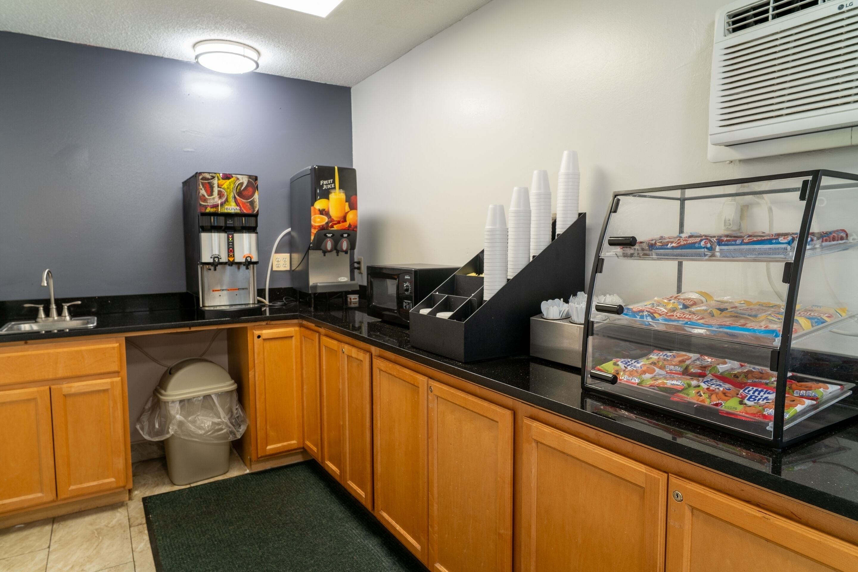 A kitchenette with a coffee machine, a juice dispenser, and a refrigerated display case with snacks.