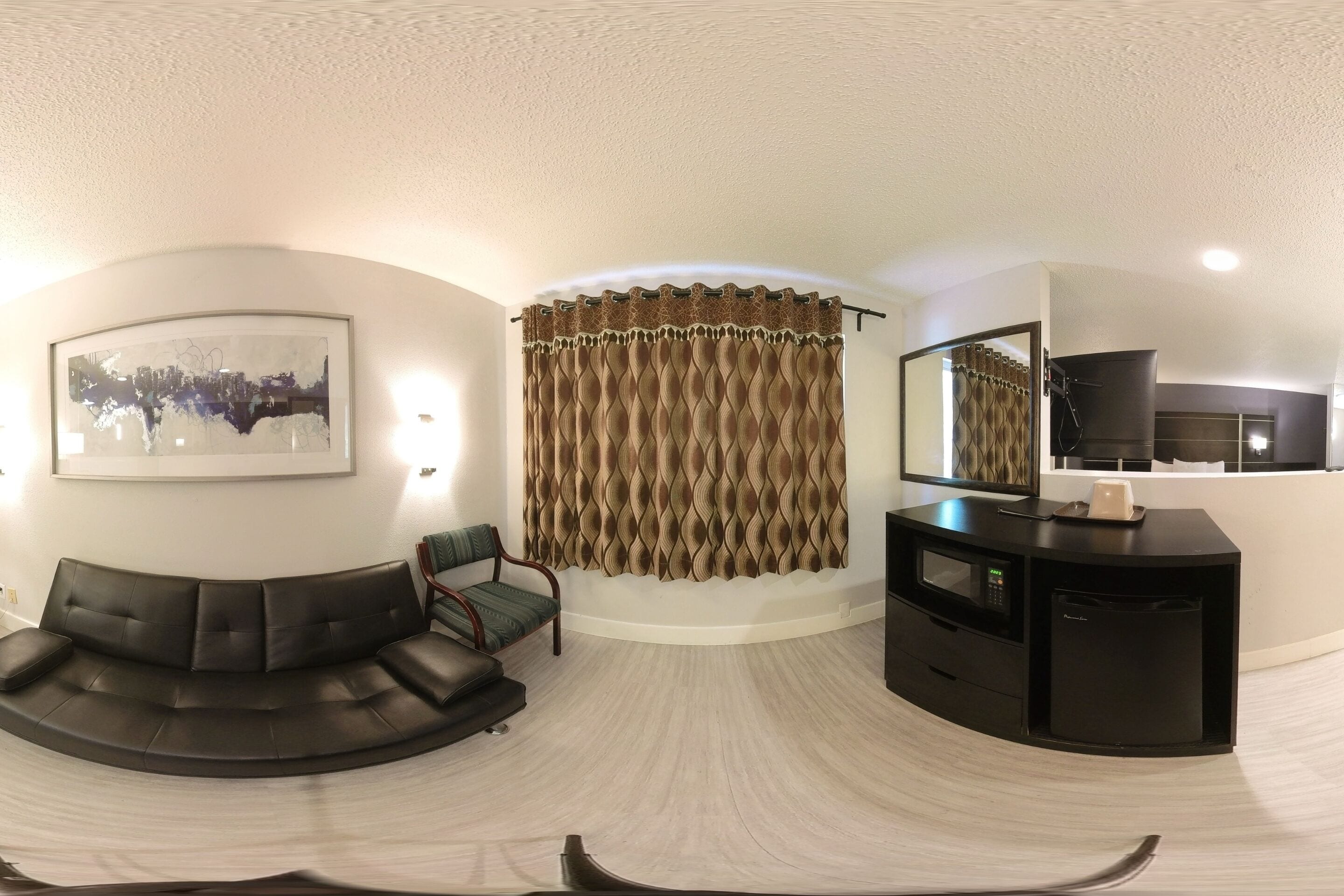 A modern living room with a curved sofa, a flat-screen TV, and a dining area with a microwave.
