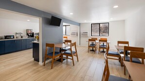Una cocina moderna con armarios azul oscuro, un televisor de pantalla plana y un comedor con mesas y sillas de madera.