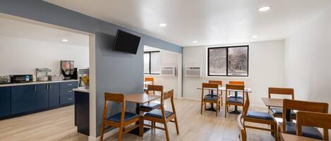 A modern kitchen with dark blue cabinets, a flat-screen TV, and a dining area with wooden tables and chairs.