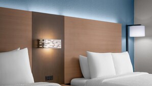 Habitación de hotel con dos camas, una lámpara fijada a la pared y una mesita de noche.