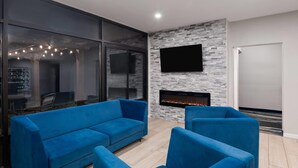 Una sala de estar moderna con chimenea, sofás azules, un televisor de pantalla plana y una pared de vidrio.