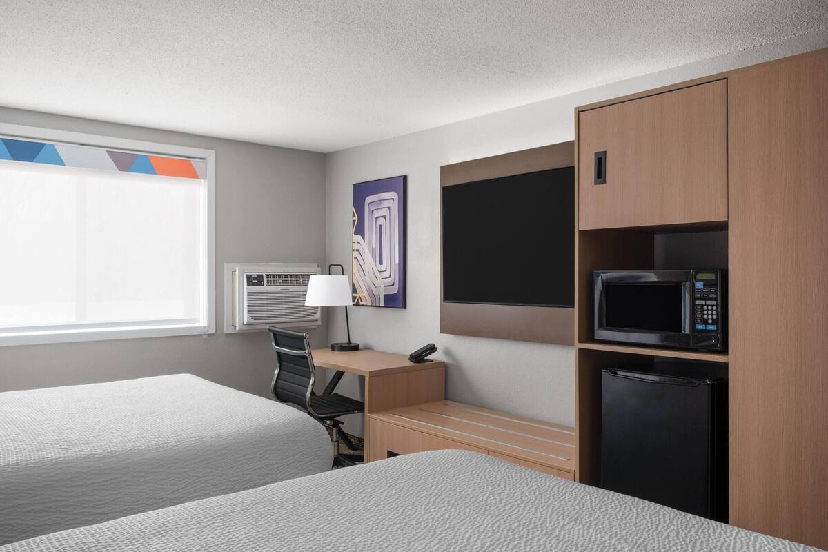 Een hotelkamer met twee bedden, een bureau, een stoel, een televisie, een magnetron en een koelkast.