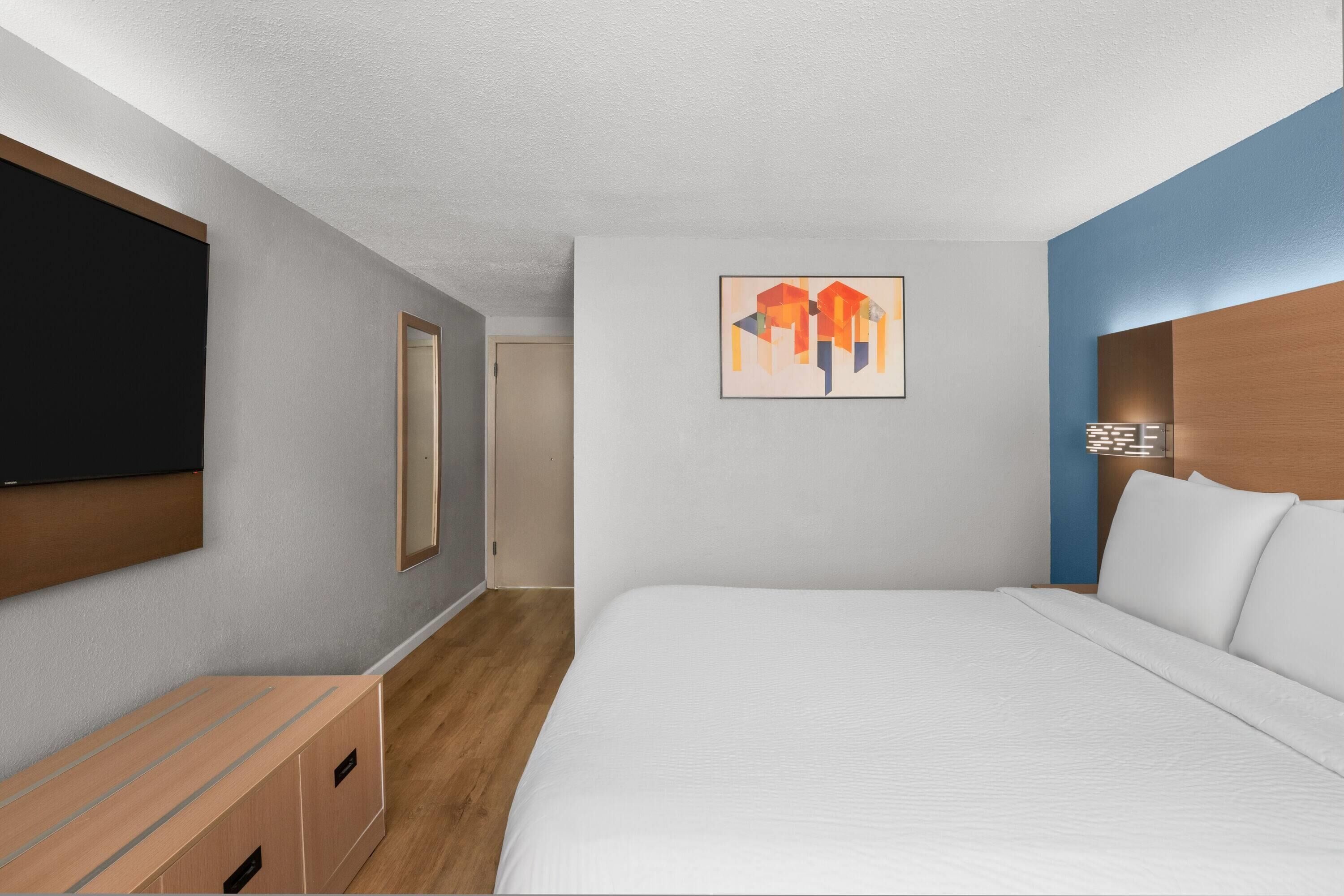 Habitación de hotel con cama, televisor de pantalla plana, cómoda de madera y una obra de arte colgada en la pared.